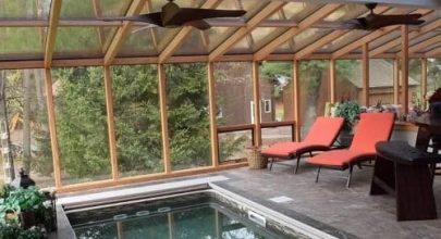 Indoor swimming pool enclosed by large glass windows, offering a panoramic view of a lush grassy field and a small shed outside