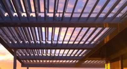 Modern sunroom roof with glass panels and metal framework at sunset.